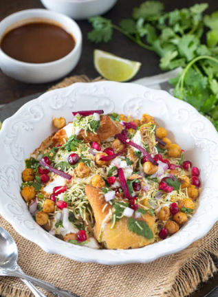 Easy homemade samosa chaat topped with chole, yogurt, sev, chutneys, onions, and coriander in a serving bowl