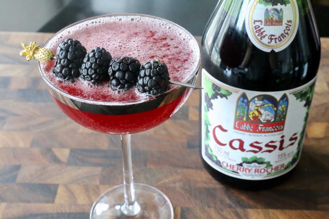 Glass of crème de cassis, a French blackcurrant liqueur, served in an elegant cocktail with fresh berries.