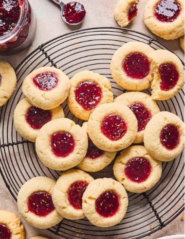 Freshly baked thumbprint cookies filled with raspberry jam on a cooling rack.