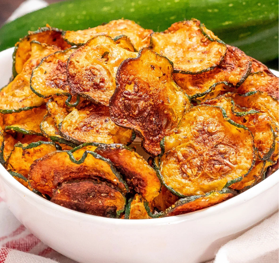 Golden, crispy air fryer zucchini chips served on a plate with a creamy dipping sauce.